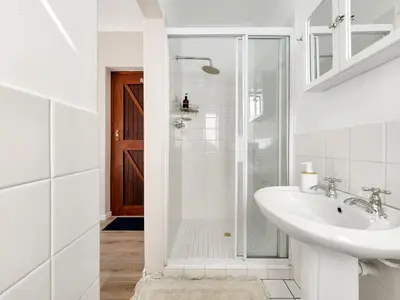 a white bathroom with a sink and a shower at Tranquil Garden Cottage in Cape Town