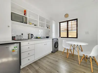 a kitchen with white cabinets and a table and chairs at Tranquil Garden Cottage in Cape Town