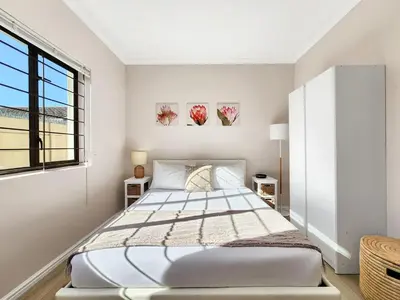 a white bedroom with a bed and a window at Tranquil Garden Cottage in Cape Town