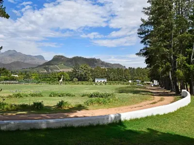 a park with a path in a field with mountains at La Jolie Dauphine Guest House in Franschhoek