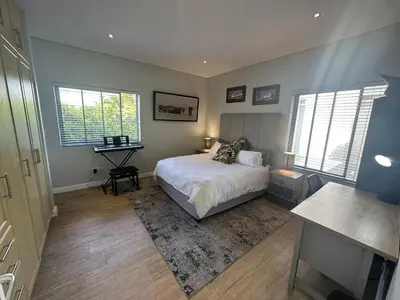 a bedroom with a bed and a desk and two windows at Sunset Links Golf Estate home, walk to Beach in Cape Town