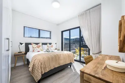 a white bedroom with a bed and a table at Esplanade Hermanus Central Sea Views in Hermanus
