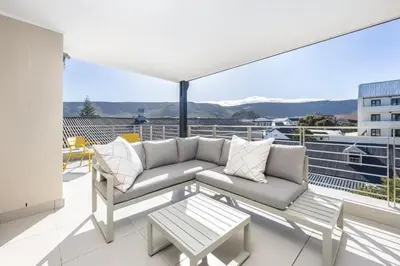 a living room with a couch and a table on a balcony at Esplanade Hermanus Central Sea Views in Hermanus