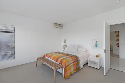 a white bedroom with a bed and a bench at Sunset Fairway Vista Villa in Cape Town
