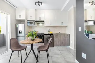 a kitchen with a table and two chairs and a kitchen with white cabinets at The Orion 18 in Table View