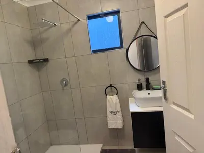 a bathroom with a shower with a mirror and a sink at Mopanie House in Brackenfell