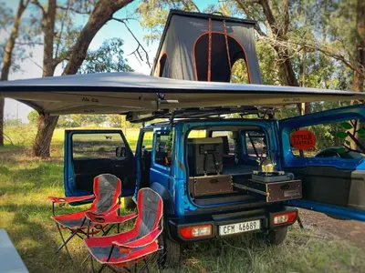 two chairs and a van with a surfboard on top at Happy Campers South Africa in Strand