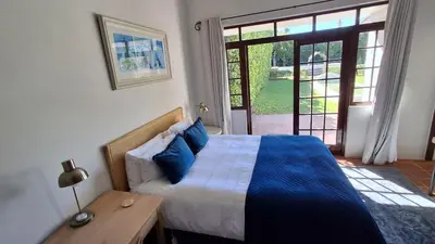 a bedroom with a bed and a table and a window at La Mode Garden Cottage in Paarl