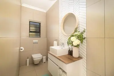 a bathroom with a sink and a mirror and a toilet at Peppertree Villa in Brackenfell