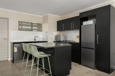 a kitchen with black cabinets and a refrigerator at Modern 2 Bed Century City Apartment, Pool and Braai in Cape Town