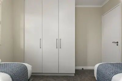 two white cabinets in a bedroom with two beds at Modern 2 Bed Century City Apartment, Pool and Braai in Cape Town