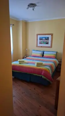 a bedroom with a large bed with colorful sheets and pillows at The Cottage, Heide Avenue in Somerset West