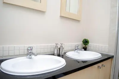 two sinks in a bathroom with two mirrors at Knightsbridge Luxury Apartments in Cape Town