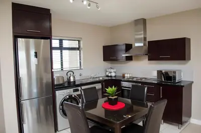 a kitchen with a table with chairs and a refrigerator at Knightsbridge Luxury Apartments in Cape Town