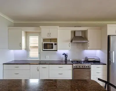 a kitchen with white cabinets and a stove top oven at Skye Cottage in Onrus River in Hermanus