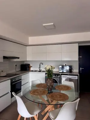 a kitchen with a glass table and white cabinets at Cosy Flat Steps from the Beach in Cape Town