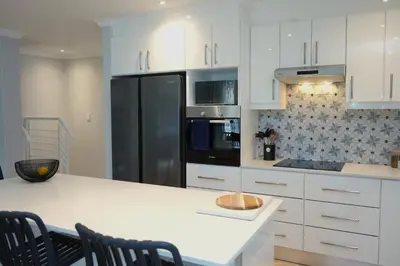 a kitchen with white cabinets and a black refrigerator at Modern Family Golf Lodge in Winelands Paradise in Paarl