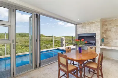 a dining room with a table and a swimming pool at Dune Pavillion Beach Villa-Where the Ocean Meets the Mountain in Cape Town