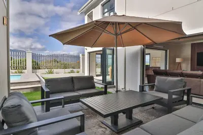 a patio with a table and chairs and an umbrella at Relax in comfort and style with a swimming pool, aircons and braai room in Hermanus
