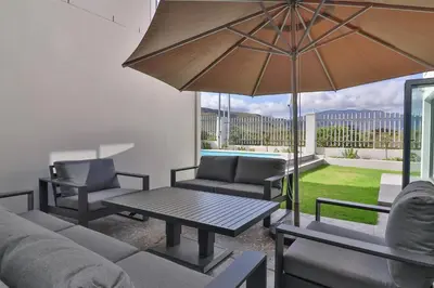 a patio with a table and chairs and an umbrella at Relax in comfort and style with a swimming pool, aircons and braai room in Hermanus