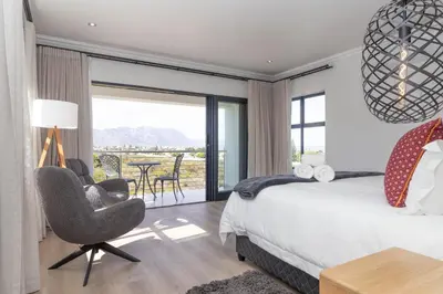 a bedroom with a bed and a chair and a table at Relax in comfort and style with a swimming pool, aircons and braai room in Hermanus