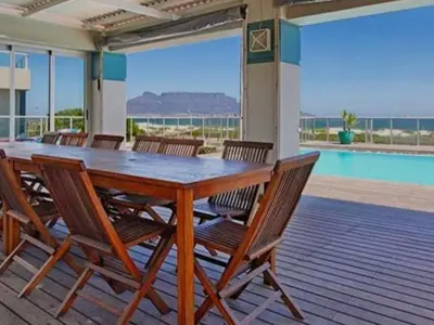 a wooden table and chairs on a deck with a pool at Cape Town Beachfront Accommodation in Blouberg in Bloubergstrand