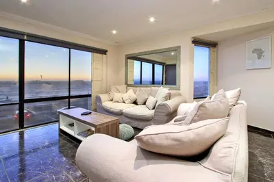 a living room with white furniture and large windows at Cap Du Mont Cape Town in Bloubergstrand