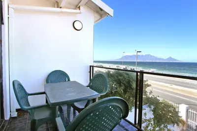 a table and chairs on a balcony with a view of the beach at Cap Du Mont Cape Town in Bloubergstrand