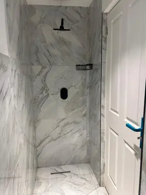 a shower with white marble walls and a door at Jorash Guesthouse in Cape Town