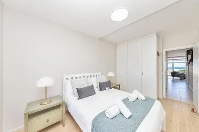 a white bedroom with a bed and a desk with a lamp at Beautiful & Modern Dolphin Beach CG12 by HMH in Cape Town