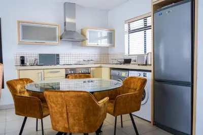 a kitchen with a table and chairs and a refrigerator at Modern 1BR Flat - Near Canal Walk in Cape Town