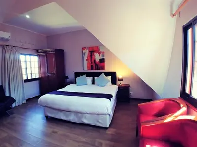 a bedroom with a large bed and a red chair at Winelands Villa Guesthouse and Cottages in Somerset West
