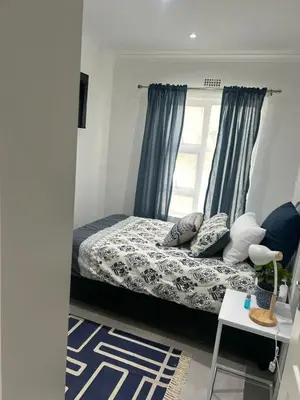 a bedroom with a bed with blue curtains and a window at Sunbird Poolhouse in Silver Sands
