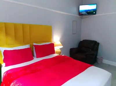 a bedroom with a bed with red pillows and a chair at Neo & Ruks Rooms Parow 5 in Goodwood