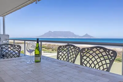a bottle of wine sitting on a table with chairs at Dolphin Beach H205 Beachfront APT, Blouberg by HMH in Cape Town