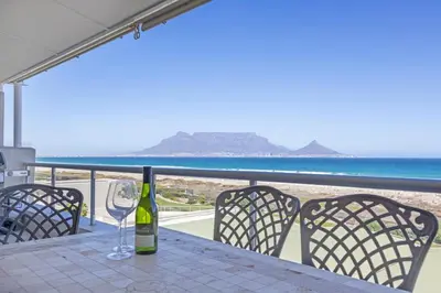 a bottle of wine sitting on a table on the beach at Dolphin Beach H205 Beachfront APT, Blouberg by HMH in Cape Town