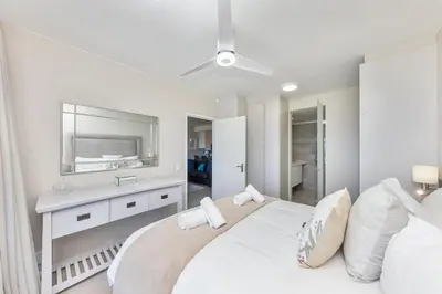a white bedroom with a large bed and a mirror at Dolphin Beach H205 Beachfront APT, Blouberg by HMH in Cape Town
