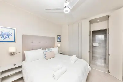 a white bedroom with a large white bed with white pillows at Dolphin Beach H205 Beachfront APT, Blouberg by HMH in Cape Town