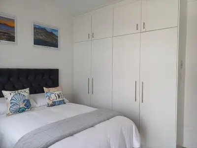 a white bedroom with a bed and white cabinets at Cozy Cove in Cape Town