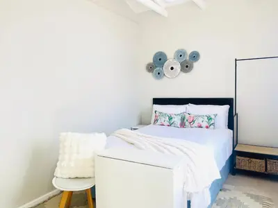 a white bedroom with a bed and a chair at Bahlaloga Studio Durbanville in Durbanville