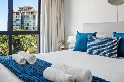 a bedroom with a bed with blue pillows and a window at La Savina The Island Club in Cape Town