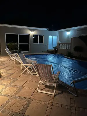 two lawn chairs sitting next to a swimming pool at night at Somerset West All Stay 4 in Somerset West