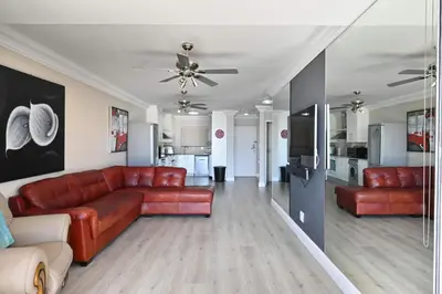 a living room with a red couch and a kitchen at Beautiful Views - Lagoon Beach 2 Bed Apartment in Cape Town