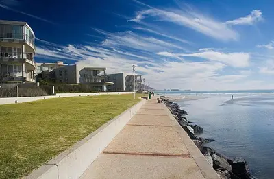 a walkway next to the beach with buildings and the water at Beautiful Views - Lagoon Beach 2 Bed Apartment in Cape Town