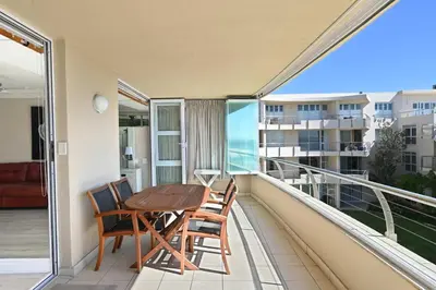 a balcony with a wooden table and chairs at Beautiful Views - Lagoon Beach 2 Bed Apartment in Cape Town