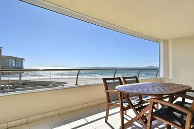 a table and chairs on a balcony with a view of the ocean at Beautiful Views - Lagoon Beach 2 Bed Apartment in Cape Town