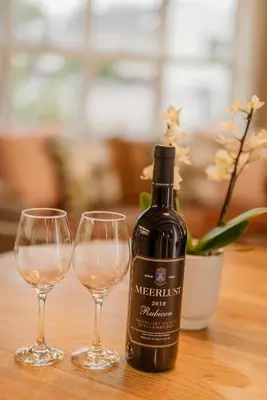 a bottle of wine next to two glasses on a table at Protea Garden Cottage in Stellenbosch