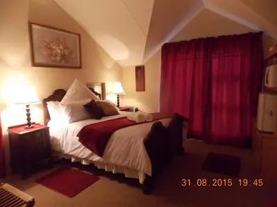 a bedroom with a large bed with red curtains at Avondsrus Guesthouse in Bettyʼs Bay