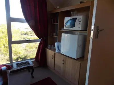 a room with a tv on a shelf with a window at Avondsrus Guesthouse in Bettyʼs Bay