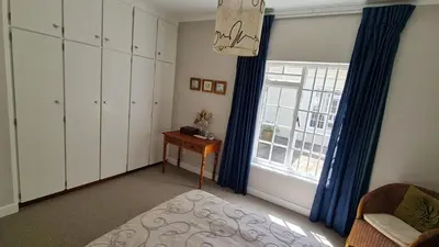 a bedroom with a bed and a window with blue curtains at Tranquil Stylish Home with Nature Pool near Reserve in Somerset West